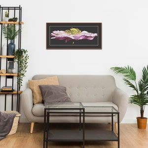 K&ouml;nnte beinhalten: Ein gerahmtes Kreuzstich-Kunstwerk, das eine gro&szlig;e, rosafarbene Blume mit gelber Mitte zeigt. Das Kunstwerk h&auml;ngt an einer wei&szlig;en Wand &uuml;ber einem grauen Sofa mit zwei Kissen.