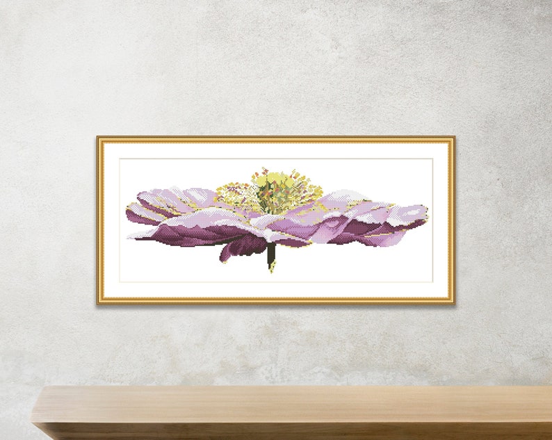 K&ouml;nnte beinhalten: Eine gerahmte Kreuzstich-Stickerei einer einzelnen, gro&szlig;en, lila Blume mit gelber Mitte. Die Blume ist in einem realistischen Stil dargestellt.