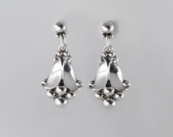 Puede incluir: Un par de pendientes de plata con diseño floral. Los pendientes tienen un racimo de pequeñas cuentas redondas en la parte inferior.