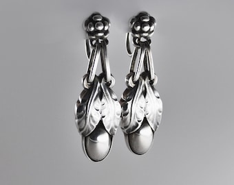 Puede incluir: Un par de pendientes de plata con diseño floral y una gota de perla.