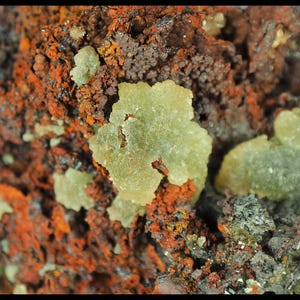 May include: Detailed image of a mineral sample, showcasing a variety of textures and colours. The main shades are rusty orange and brown, with areas of pale green, possibly crystalline structures. The overall look is rugged and natural.