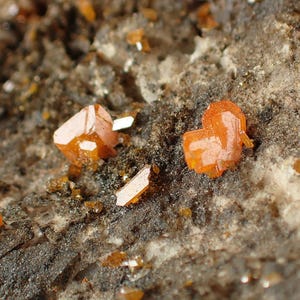 Puede incluir: Primer plano de cristales naranjas sobre una roca marrón oscura. Los cristales son afilados y tienen un aspecto vítreo.