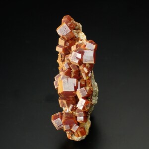 May include: A cluster of orange-red vanadinite crystals on a matrix. The crystals are sharp and well-formed, with a glassy lustre.