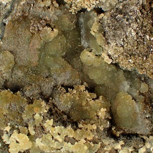 May include: Close-up of a mineral specimen with a variety of colours and textures. The image shows a combination of light green, brown, and tan hues. The mineral appears to have a crystalline structure, with various formations and surface details.