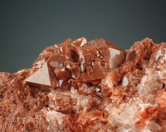 May include: A cluster of reddish-brown quartz crystals on a matrix of brown rock. The crystals are sharp and well-formed, with a glassy luster.