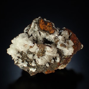 Puede incluir: Un espécimen mineral que presenta un grupo de estructuras cristalinas blancas y translúcidas incrustadas en una matriz oscura, texturizada y de color marrón rojizo. La formación muestra un contraste entre la base dentada de aspecto metálico y las puntas de cristal geométricas, claras y afiladas, que sobresalen de la superficie de la roca.