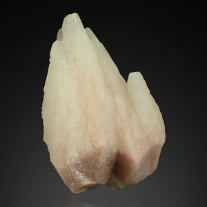 May include: A natural mineral specimen featuring a cluster of crystalline formations. The stone has a pale, creamy color with hints of pink and brown at the base. The overall shape is irregular and textured, with sharp edges and a rough surface.