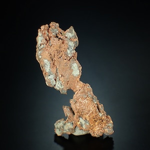 Peut inclure: Un gros morceau de minerai de cuivre de forme irrégulière avec une surface rugueuse et texturée. Le cuivre est de couleur brun rougeâtre et présente un éclat métallique. Le minerai est partiellement recouvert d'une substance blanche et poudreuse.