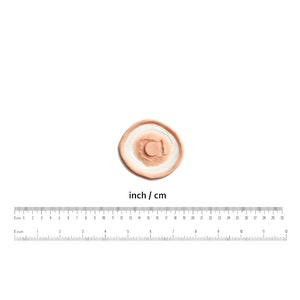 Op de afbeelding: Een kleine, ronde, huidkleurige siliconenprothese met een verhoogd, cirkelvormig, bruin centrum. De prothese is ontworpen om een ​​wond of verwonding na te bootsen.