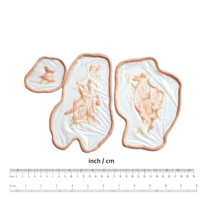 May include: Three prosthetic wound appliances with a flesh-toned color, each with a textured surface and a thin, light-brown border. The appliances are on a white background, with a ruler showing inches and centimeters.