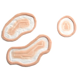 May include: Three beige-colored silicone practice wound pads with different shapes and designs. The pads are designed to simulate various types of wounds, such as cuts, abrasions, and punctures.