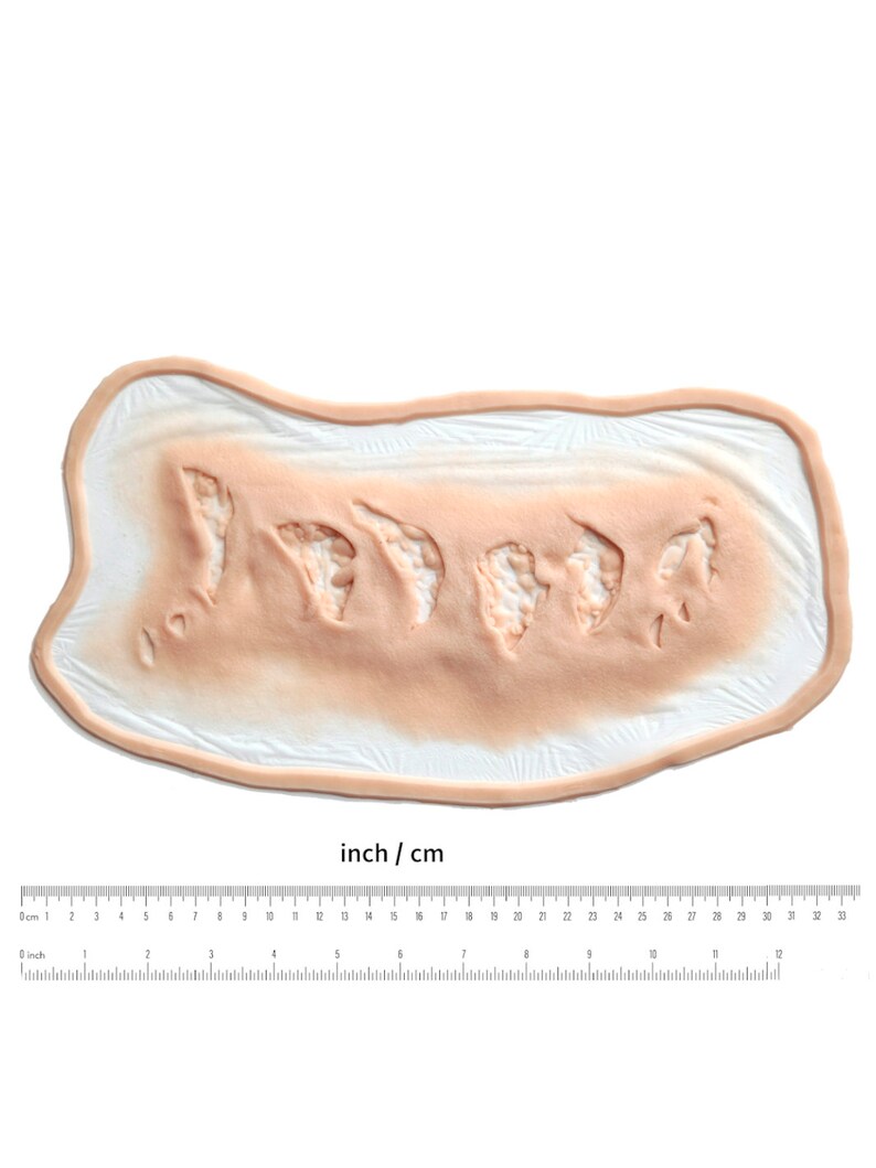 Puede incluir: Primer plano de una herida falsa de aspecto realista, hecha de silicona, con una superficie texturizada y un borde irregular. La herida mide aproximadamente 18 cm de largo y 5 cm de ancho.