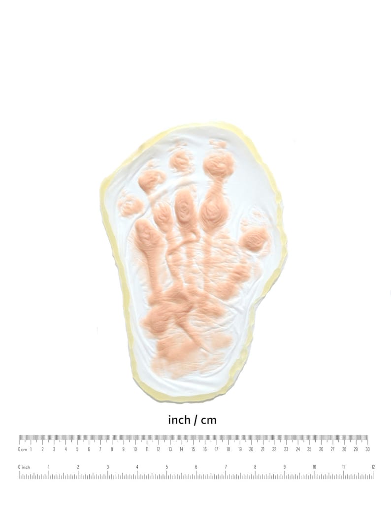 May include: A white plaster handprint mold with a light pink impression of a hand. The mold is approximately 6 inches in diameter.
