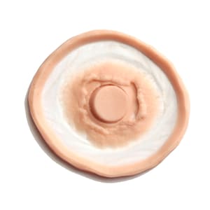 Op de afbeelding: Een ronde, huidkleurige siliconen mal met een verhoogd, cirkelvormig ontwerp in het midden. De mal is ontworpen om realistisch ogende nep-wonden te cre&euml;ren.