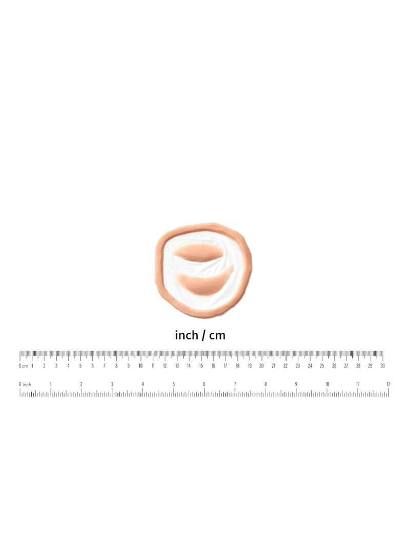 Puede incluir: Primer plano de un peque&ntilde;o molde de silicona redondo de color carne con dos impresiones ovaladas en relieve. El molde est&aacute; dise&ntilde;ado para crear heridas de aspecto realista para el maquillaje de efectos especiales.