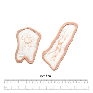 May include: Two silicone moulds for making resin crafts. The moulds are shaped like a long, thin rectangle and a short, wide rectangle. The moulds are made of a clear silicone material and have a light pink colour.