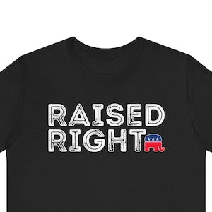 May include: Black t-shirt with the words "RAISED RIGHT" in white block letters. The word "RIGHT" has a small red, white, and blue graphic of an elephant. The shirt is made of a soft material.