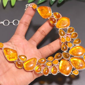 May include: A silver necklace with a series of amber-coloured, irregularly shaped stones. The stones vary in size and shape, with a polished, glossy finish. The necklace is displayed against a dark background.