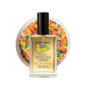 May include: A perfume bottle with a black cap and a clear rectangular body. The label reads "BLOOM • BARREL FRUITY PEBBLES CITRUS COTTON CANDY CARAMEL Eau de Parfum VOL 1.0 fl. oz." The bottle is set against a background of colorful cereal.