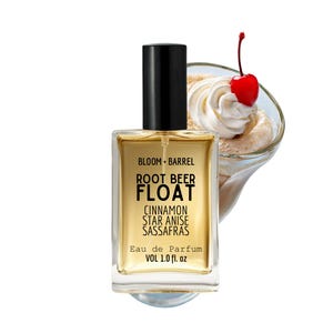 May include: A rectangular perfume bottle with a black cap and gold label. The label reads "BLOOM + BARREL ROOT BEER FLOAT CINNAMON STAR ANISE SASSAFRAS Eau de Parfum VOL 1.0 fl. oz." A root beer float with whipped cream and a cherry is in the background.