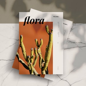 May include: A magazine cover with the title "flora" in a bold, black font. The cover features a close-up of a green cactus plant against a bright orange background. The text "VOLUME 1" is in the top right corner.