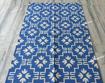 Pode incluir: Um tapete de algodão azul e branco com um padrão geométrico. O tapete tem um fundo branco com formas geométricas azuis e desenhos florais brancos.