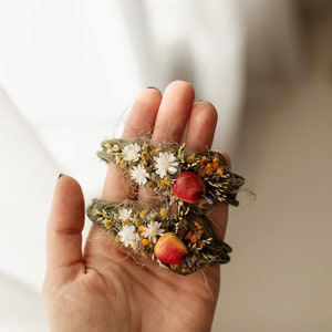 May include: Two green fabric headbands decorated with dried flowers, including white daisies, yellow flowers, and red berries.