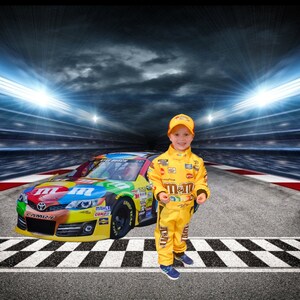 Op de afbeelding: Een jonge jongen in een geel racepak met het M&M's-logo staat voor een raceauto met het M&M's-logo. De auto staat op een racecircuit met een geblokte finishlijn.