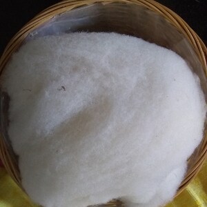 May include: A round, woven basket filled with a large mass of fluffy, white material. The basket is made of light brown woven strips and is lined with clear plastic. The white material appears soft and cloud-like.
