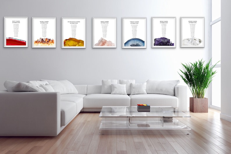 May include: Seven framed prints with white mounts and white frames, each featuring a different coloured crystal with a list of chakra attributes. The prints are hanging on a white wall above a white sectional sofa and a glass coffee table.