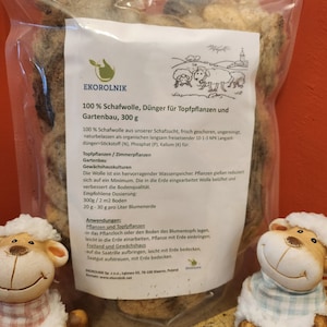 Może przedstawiać: Biały worek z obrazkiem owiec. Worek zawiera 100% wełny owczej do nawożenia roślin. Tekst na worku brzmi "100% Schafwolle, Dünger für Topfpflanzen und Gartenbau, 300 g".