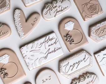 May include: A collection of 12 decorated cookies with various designs, including a heart, a ring, a rose, and the names "Alex and Jackie". The cookies are decorated in shades of brown and white.