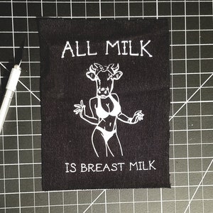 May include: Black patch with white text and a cow wearing a bikini. The text reads "ALL MILK IS BREAST MILK".