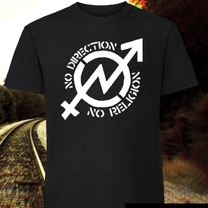 Puede incluir: Camiseta negra con un gráfico blanco de un círculo con un rayo dentro y las palabras "No Direction No Religion" alrededor. El gráfico también incluye un símbolo de género.