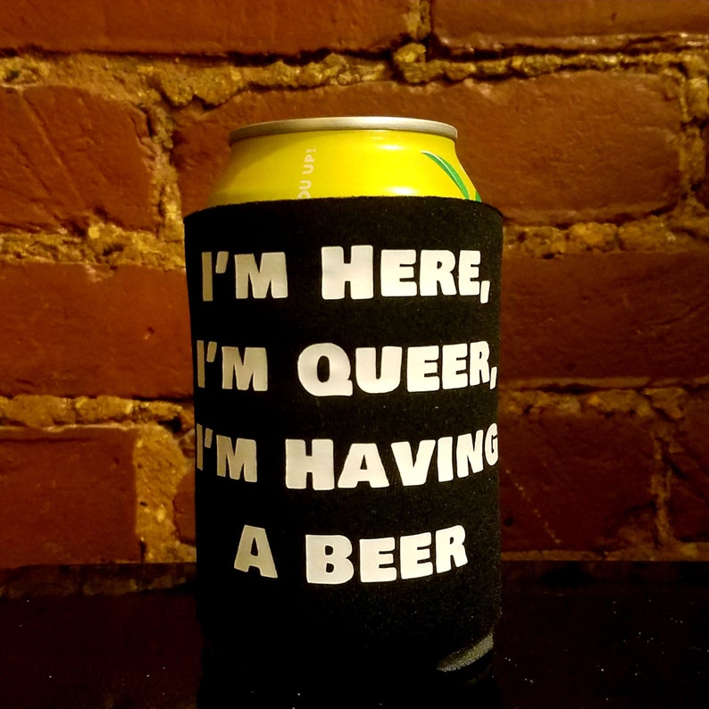 May include: Black and white can cooler with the text "I'm here, I'm queer, I'm having a beer".