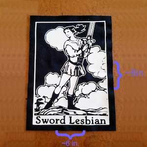 Könnte beinhalten: Schwarz-weißes Bügeleisen-Patch mit einer Frau, die ein Schwert hält und auf Wolken steht. Der Text "Sword Lesbian" ist unter dem Bild gedruckt. Das Patch ist etwa 15 cm breit und 20 cm hoch.