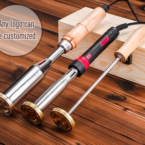 Puede incluir: Tres hierros para marcar madera con cabezas de metal y mangos de madera se muestran sobre una superficie de madera. Los hierros para marcar tienen un diseño circular en la cabeza de metal. El texto "Any logo can be customized" está en la esquina superior izquierda.