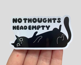 May include: A black cat sticker with the words "NO THOUGHTS HEAD EMPTY" in bold, white letters. The cat is lying on its back with its paws in the air, and its eyes are wide open. The sticker has a white border.