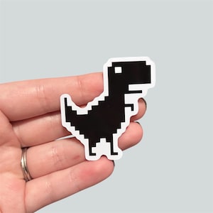 May include: Black and white pixelated dinosaur sticker. The dinosaur is in a running pose with its mouth open.
