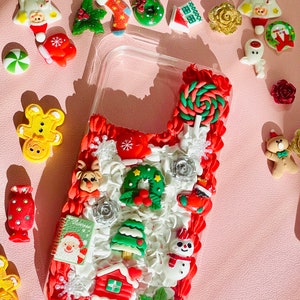 May include: A clear phone case decorated with a Christmas theme. The case is filled with red, white, and green 3D ornaments, including a snowman, a Christmas tree, a house, a candy cane, and a wreath.