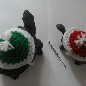 May include: Two crocheted turtle shells, one green and white, the other red and white, with a white pom-pom on top. loolapets@etsy.com