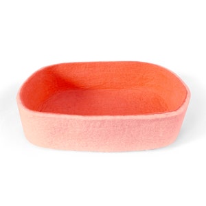 May include: A light pink felt storage basket with a rounded oval shape. The basket is empty and ready to hold items.