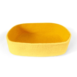 May include: A yellow felt pet bed in the shape of an oval. The bed is empty and ready for a pet to relax in.