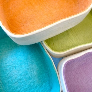 Op de afbeelding: Vier felten opbergmanden in verschillende kleuren: oranje, groen, blauw en paars. De manden zijn op elkaar gestapeld.