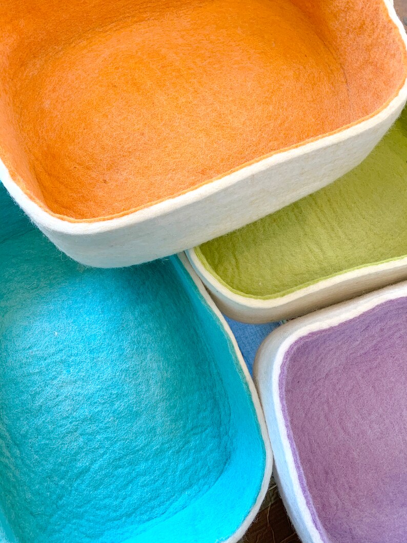 Op de afbeelding: Vier felten opbergmanden in verschillende kleuren: oranje, groen, blauw en paars. De manden zijn op elkaar gestapeld.