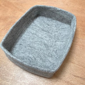 Op de afbeelding: Een rechthoekige opbergmand van grijs vilt. De mand is gemaakt van een zacht, getextureerd materiaal.