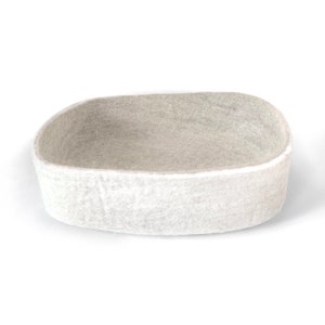 May include: A white felt oval-shaped storage basket. The basket is made of a soft, felted material and has a smooth, rounded shape.