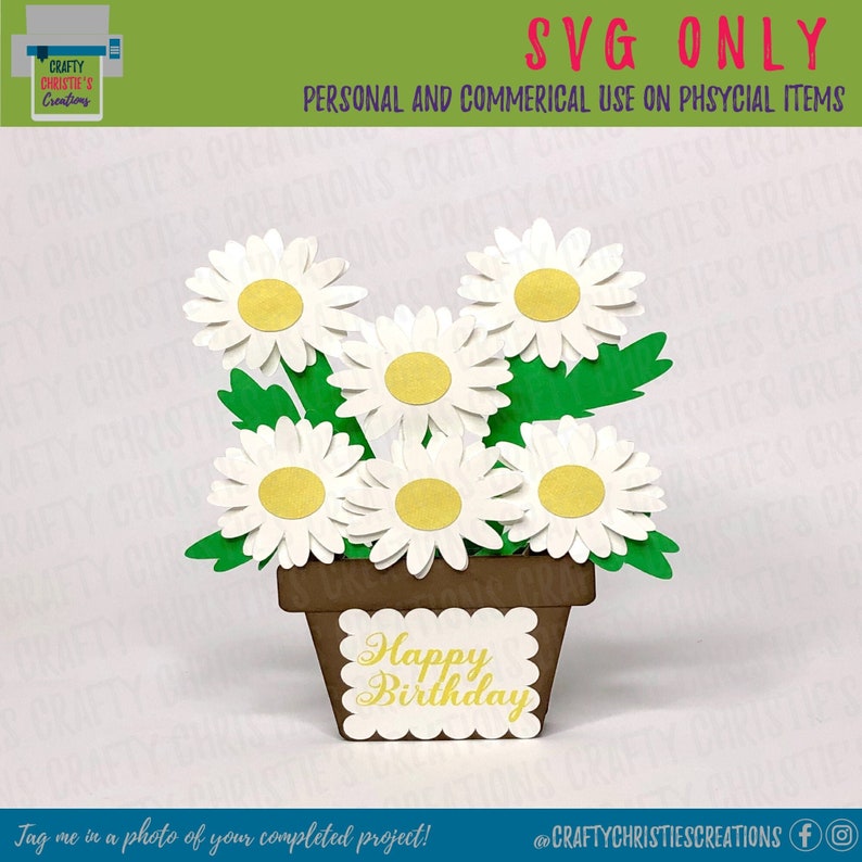 May include: A white flower pot with a brown base and a white square card with the text "Happy Birthday" in yellow letters. The pot is filled with white daisies with yellow centers.