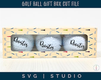 Op de afbeelding: Een geschenkdoos met drie golfballen, elk met de naam "Rooster" erop gedrukt. De doos heeft een patroon van golfclubs en tees. De tekst "GOLF BALL GIFT BOX CUT FILE" staat bovenaan.