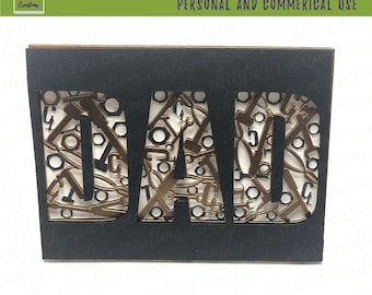 May include: Black cardstock with the word "DAD" cut out, revealing a detailed pattern of tools in gold and silver. The top right corner reads "SVG ONLY PERSONAL AND COMMERICAL USE".